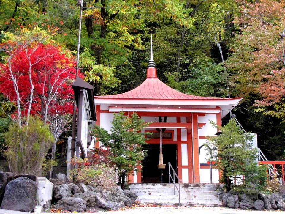 朱色の屋根のお堂と、紅く色づいた木々。手前に石段と灯籠が立つ