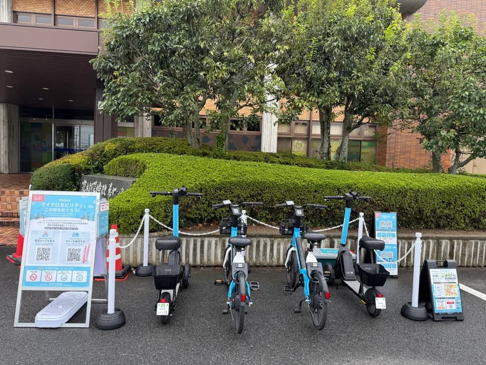 北栄町役場のポート。石碑と刈り込まれた生垣の前に TOCKLE が4台並び、左手に案内看板、手前に赤白のコーンが立つ