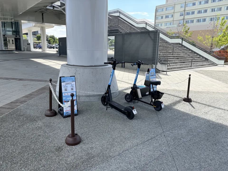 ミズウェルビーホールのポート。庇の下の白い太柱のわきに TOCKLE が2台停まり、奥に石張りの広場と階段が広がる