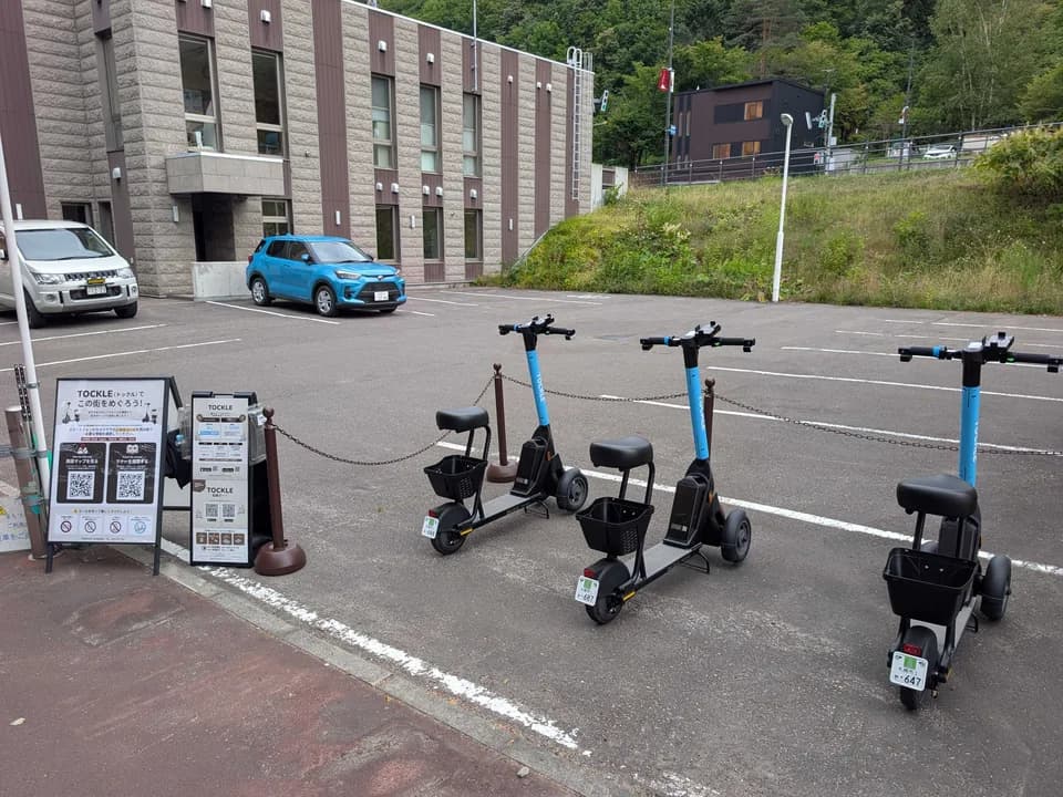 タイムズ定山渓観光駐車場のポート。区画線の引かれた駐車場に TOCKLE が3台停まり、左手に案内看板が置かれている