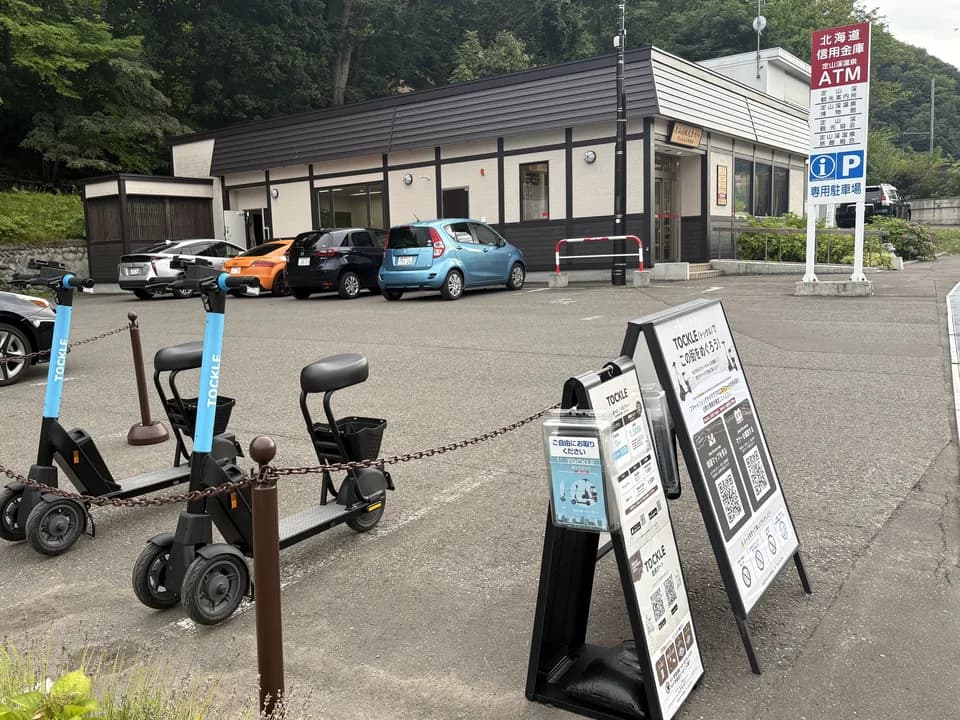 定山渓観光案内所のポート。駐車場に TOCKLE が2台停まり、その奥に観光案内所の建物と看板が見える