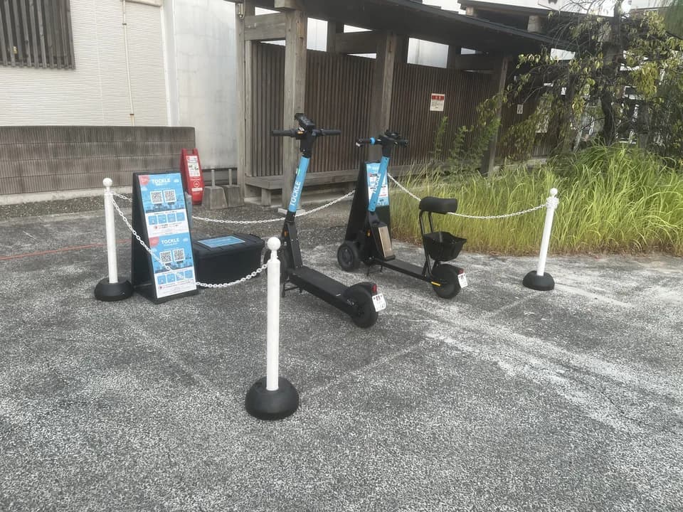 柳町入口のポート。舗装された一角に TOCKLE が2台停まり、奥に木造の門と伸びた草むらが見える