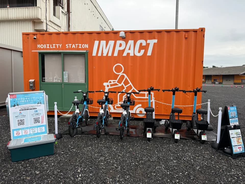 由良駅前のポート。「MOBILITY STATION IMPACT」と描かれたオレンジ色のコンテナの前に TOCKLE が6台並び、左手に案内看板が置かれている