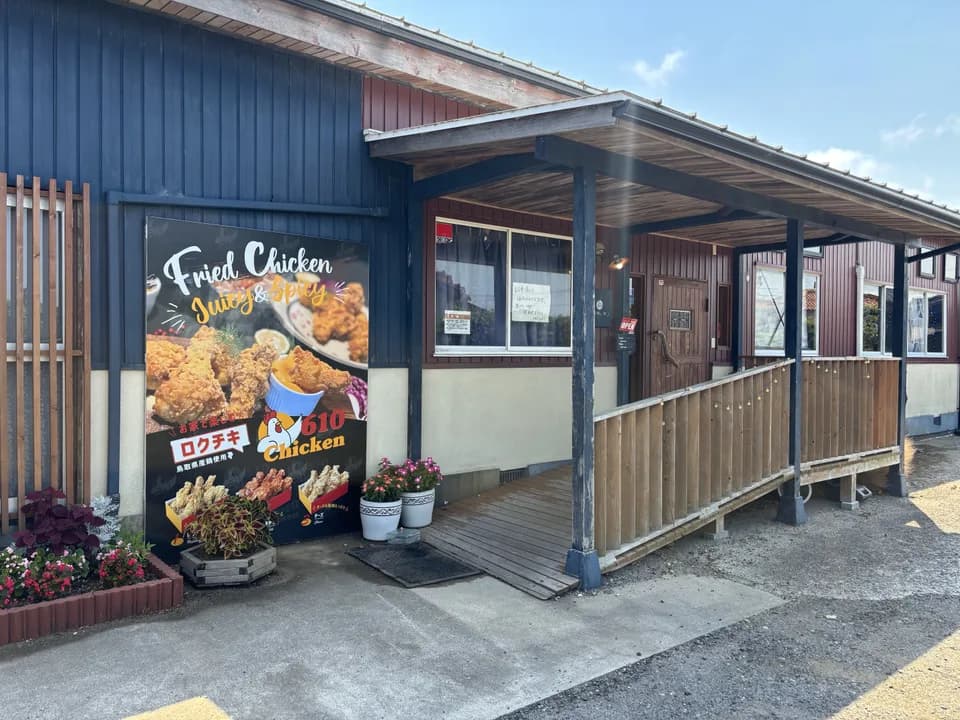 紺色の板壁の店の前。左手に「610 Chicken」の大きなから揚げの看板、右手に木の柱が並ぶひさしと、板張りのスロープが付いた入口