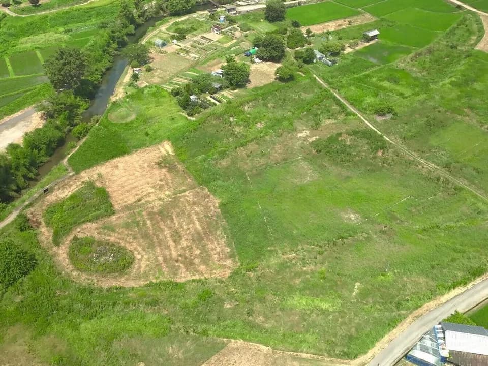 飛鳥京跡苑池一帯を上空から見たところ。草に覆われた広い平地の左手に小川が流れ、周囲に畑や民家が点在する