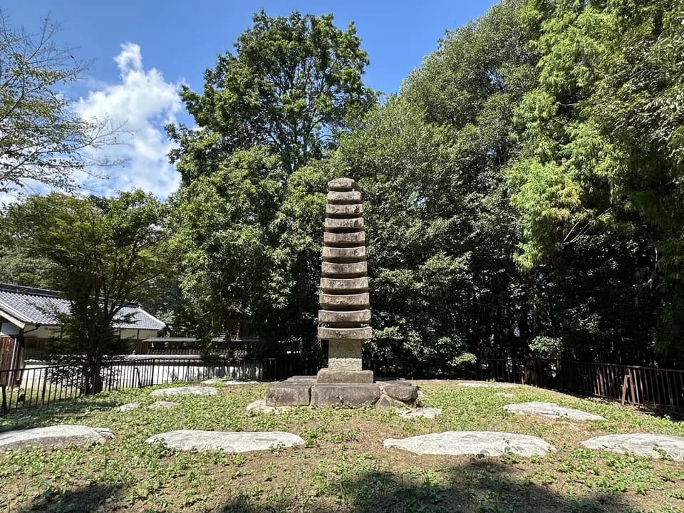 檜隈寺跡に立つ石造の塔を正面から見たところ。何層にも重なる石の塔が苔むした地面に建ち、周囲を濃い緑の木々と鉄柵が囲む