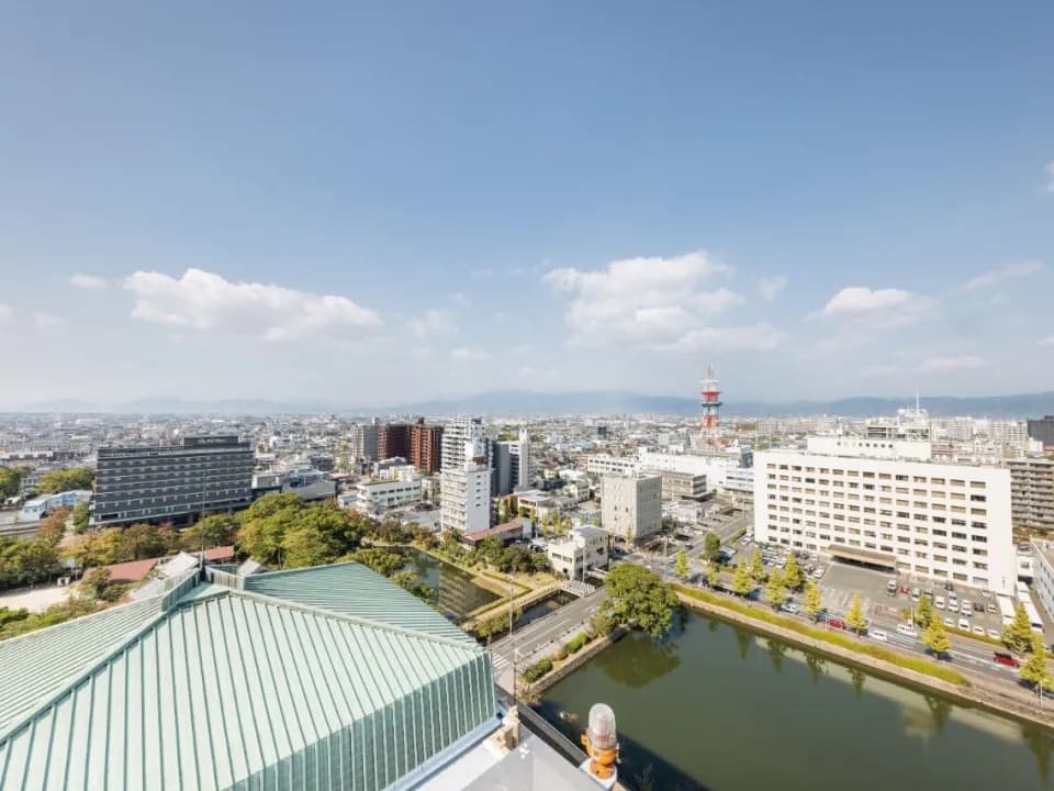 展望ホールから見下ろす佐賀の街並み。手前に緑青色の屋根とお堀、遠くまで低い家並みが広がり、奥にうっすら山並みが見える