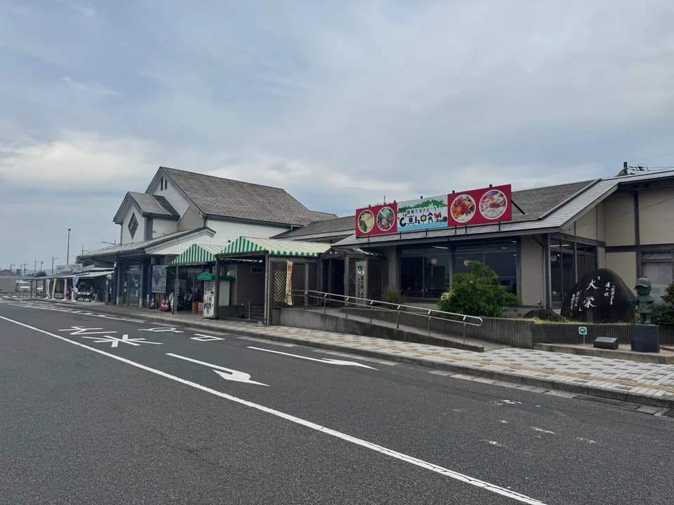 道路ぞいに建つ道の駅大栄。緑の縞のテントが張られた売店と、赤い食堂の看板、右手に「道の駅 大栄」と刻まれた石碑とコナンの像